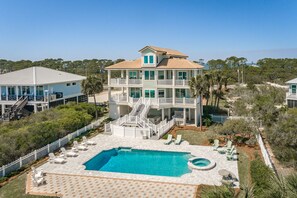 A multi-story beachfront property with a swimming pool, outdoor seating, and a view of the ocean.