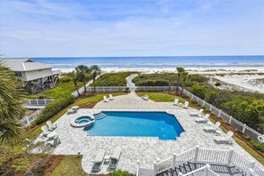 A pool area with a view of the beach, surrounded by a white fence and palm trees.