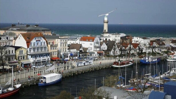 Een kustplaats met een opvallend baken, een jachthaven met verschillende boten, en gebouwen langs de oever.