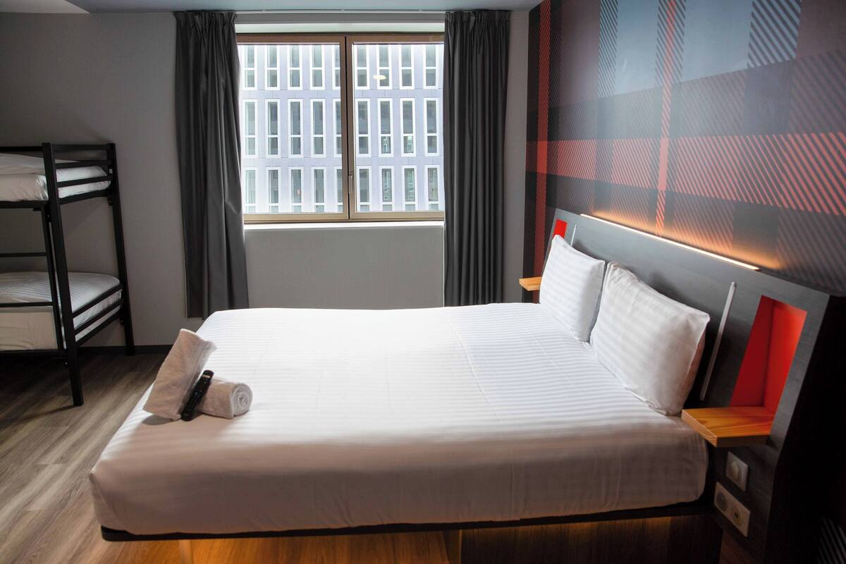 Hotelkamer met een groot bed, een stapelbed, een raam met gordijnen en een modern wandontwerp.