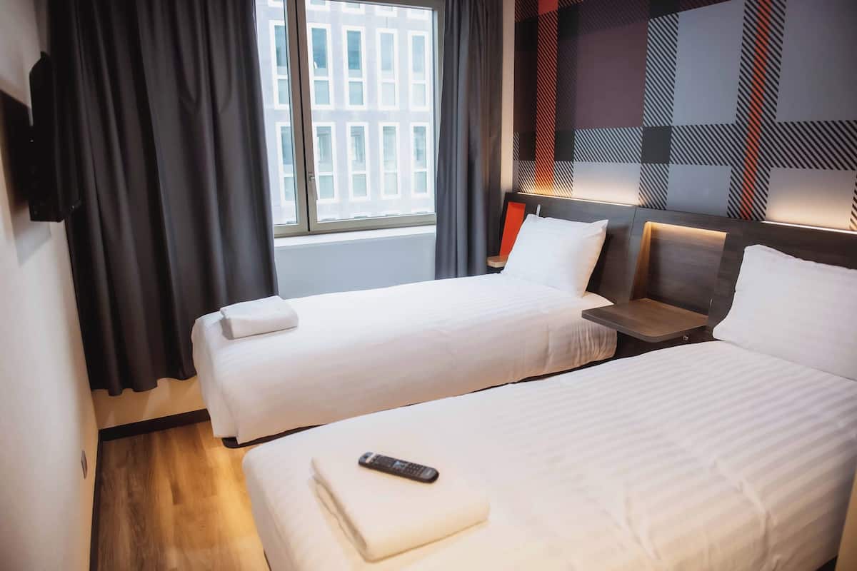 Een hotelkamer met twee bedden, een televisie, een raam met gordijnen en een behang met een patroon.