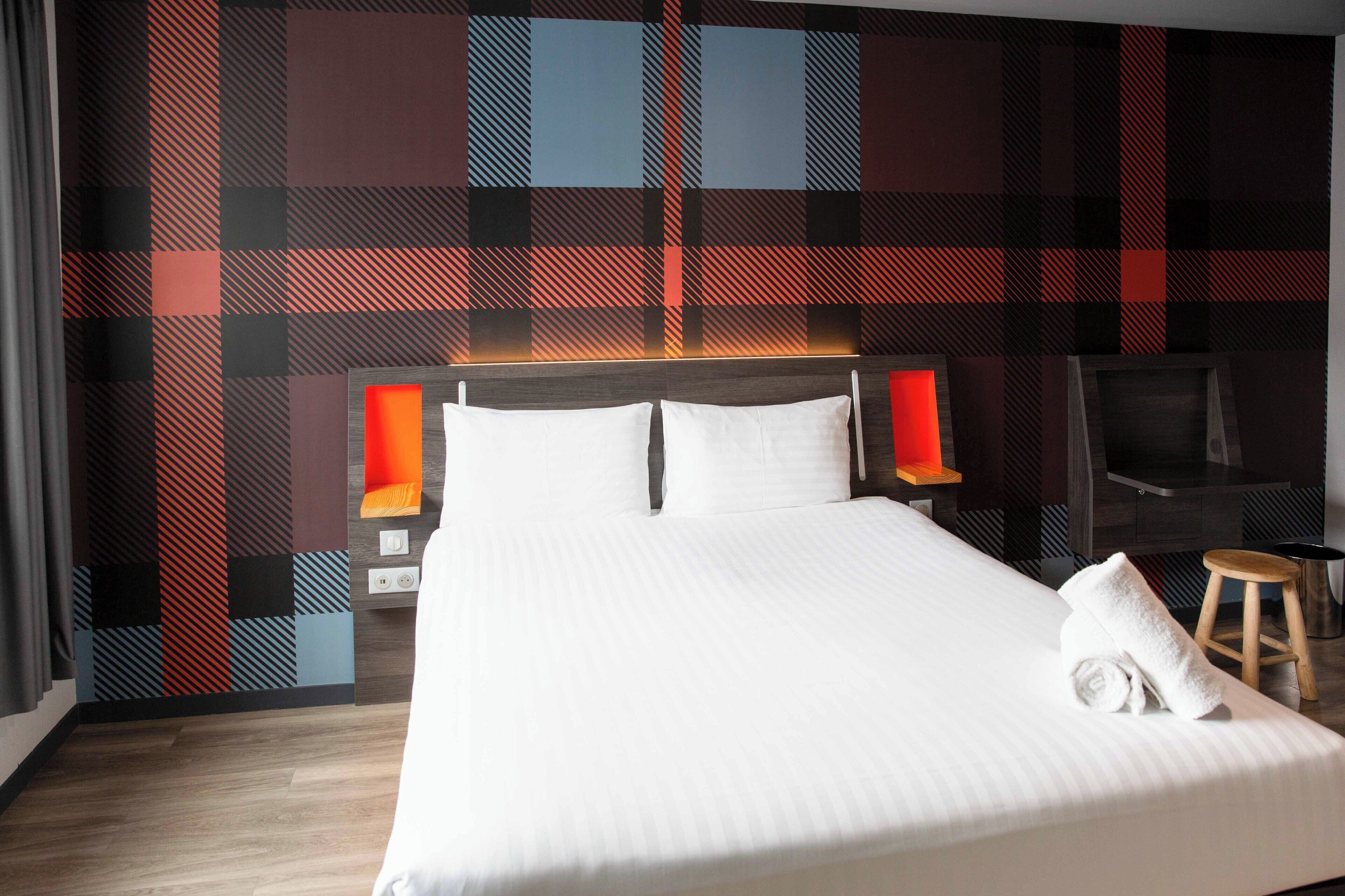 A hotel room with a large bed, two bedside tables, a TV, and a plaid-patterned wall.