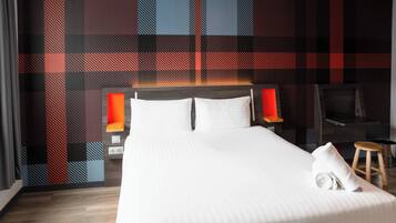 A hotel room with a large bed, two bedside tables, a TV, and a plaid-patterned wall.