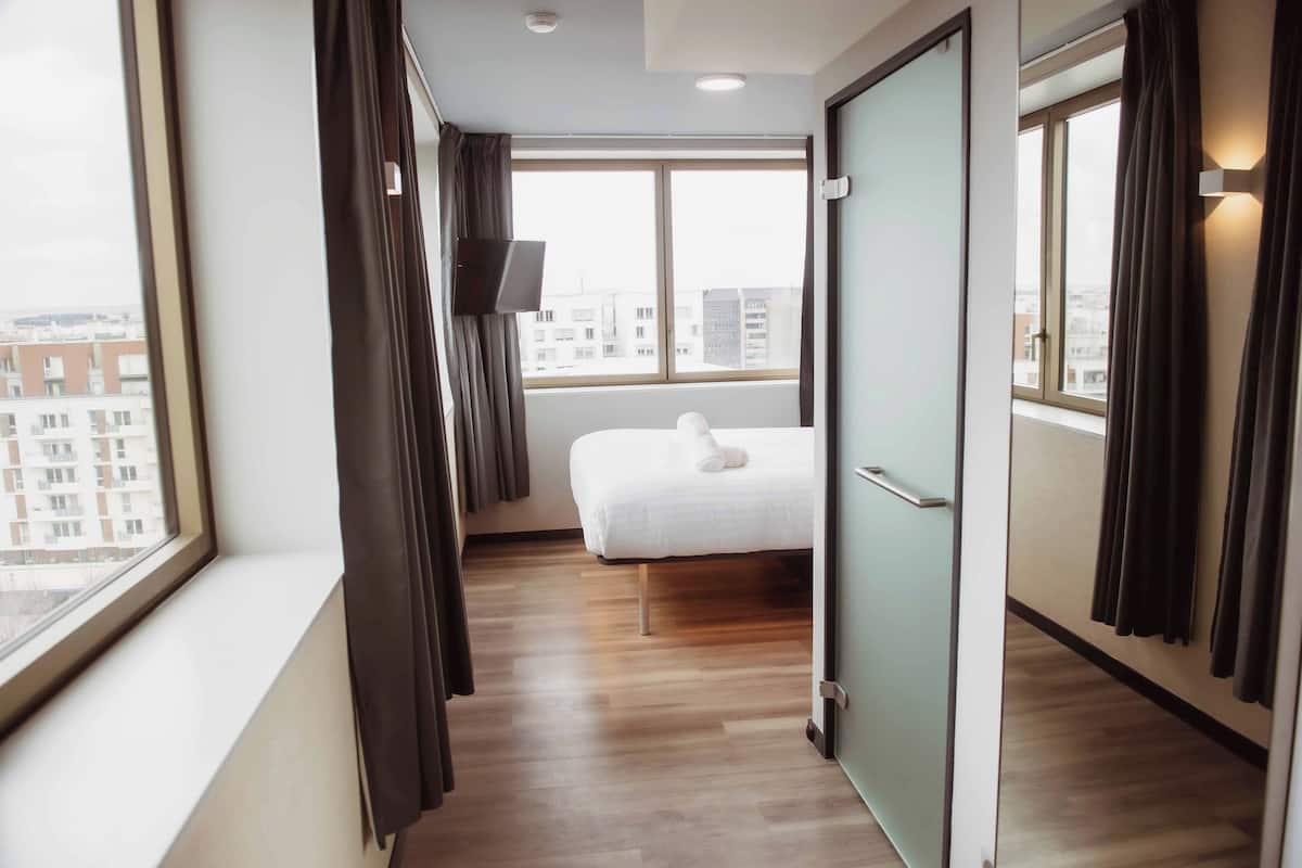 Een hotelkamer met een bed, een raam, een televisie en uitzicht op de stad.