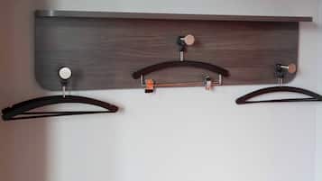 A wall-mounted wooden shelf with three black hangers.