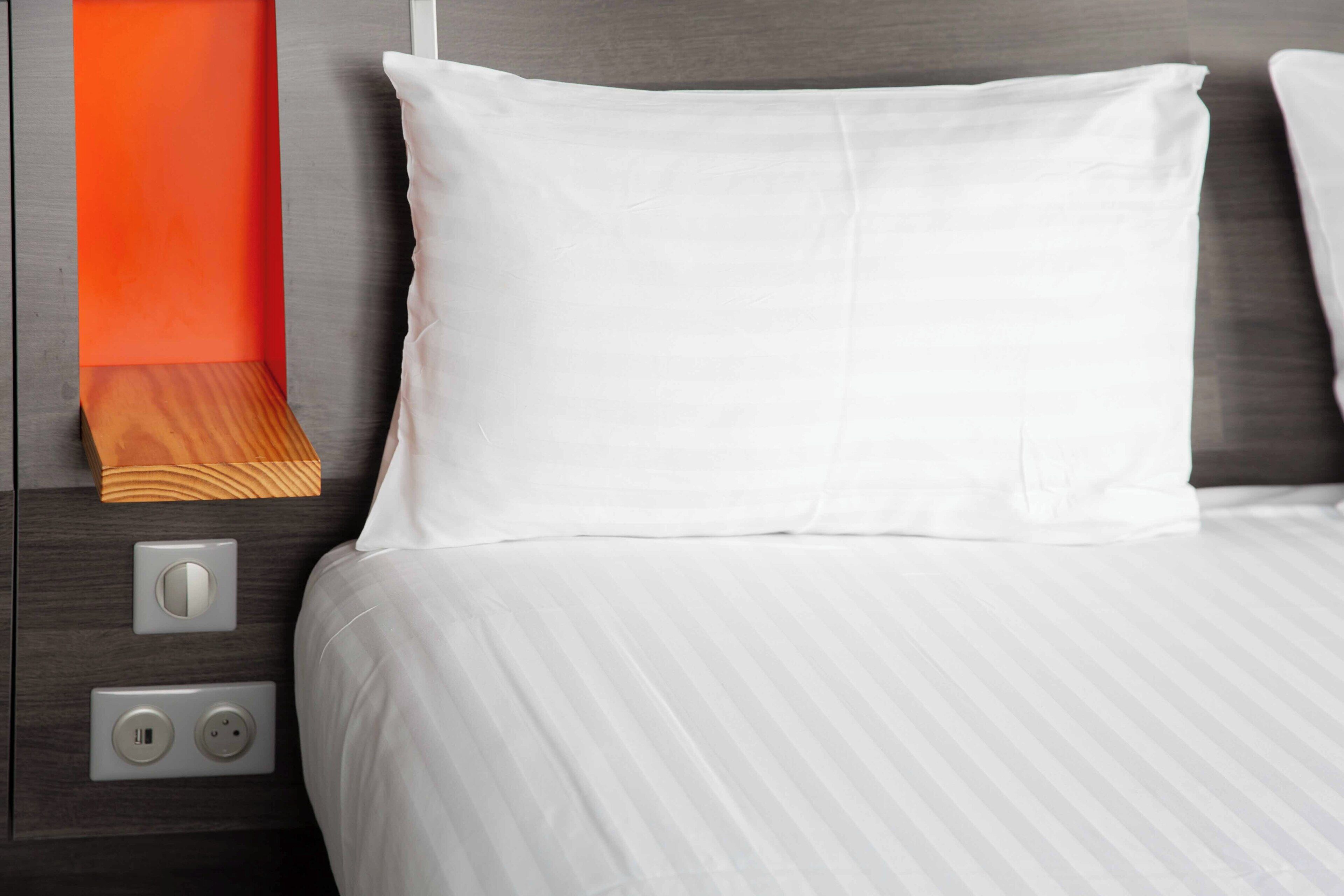 A neatly made bed with white linens, a wooden headboard, and a nightstand with a power outlet and USB port.