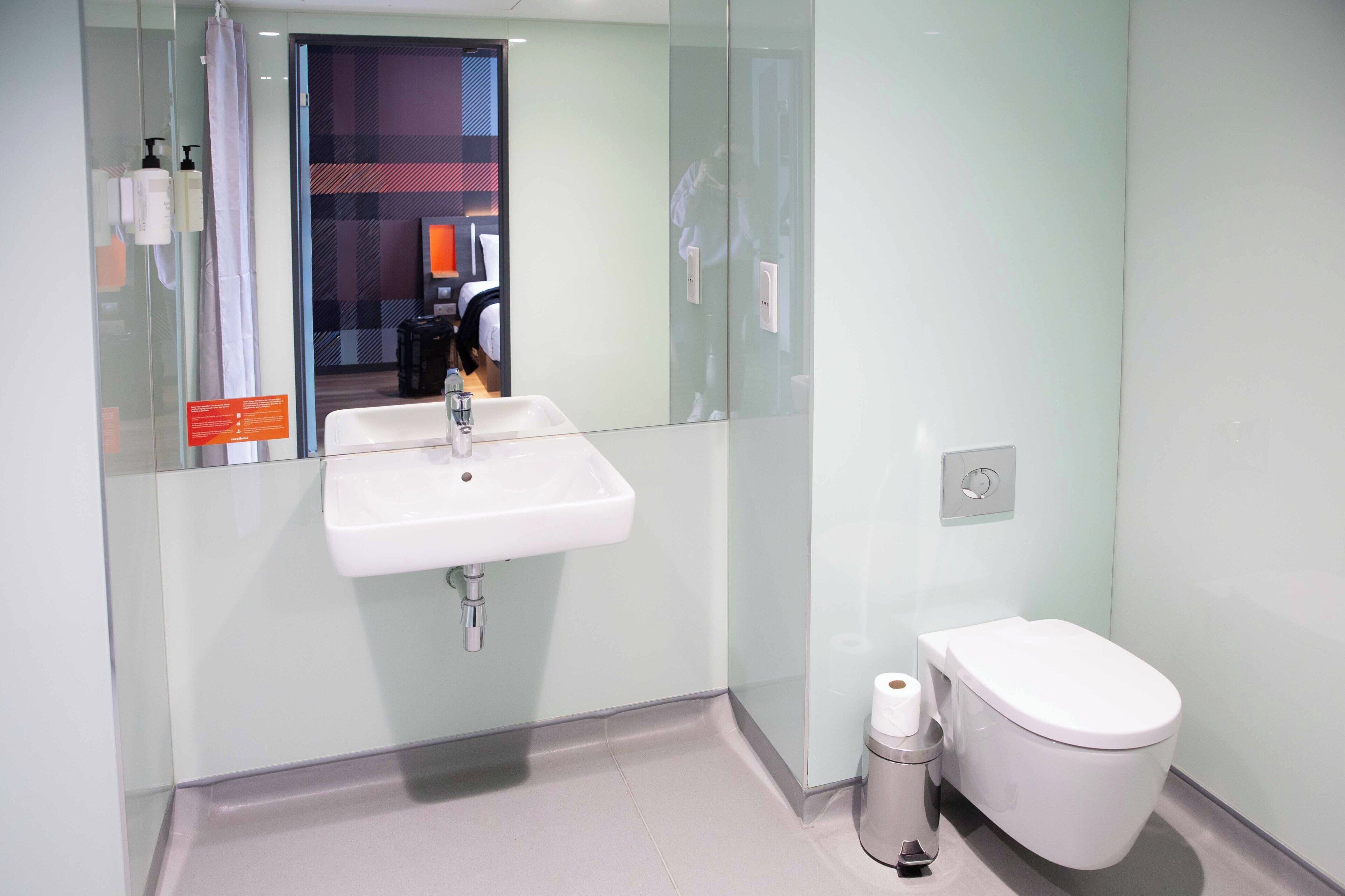 Un baño moderno con mampara de vidrio, lavamanos blanco y un inodoro.