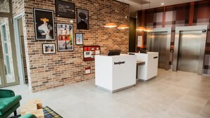 A reception area with a brick wall, framed pictures, a 'bonjour' desk, and two elevators.