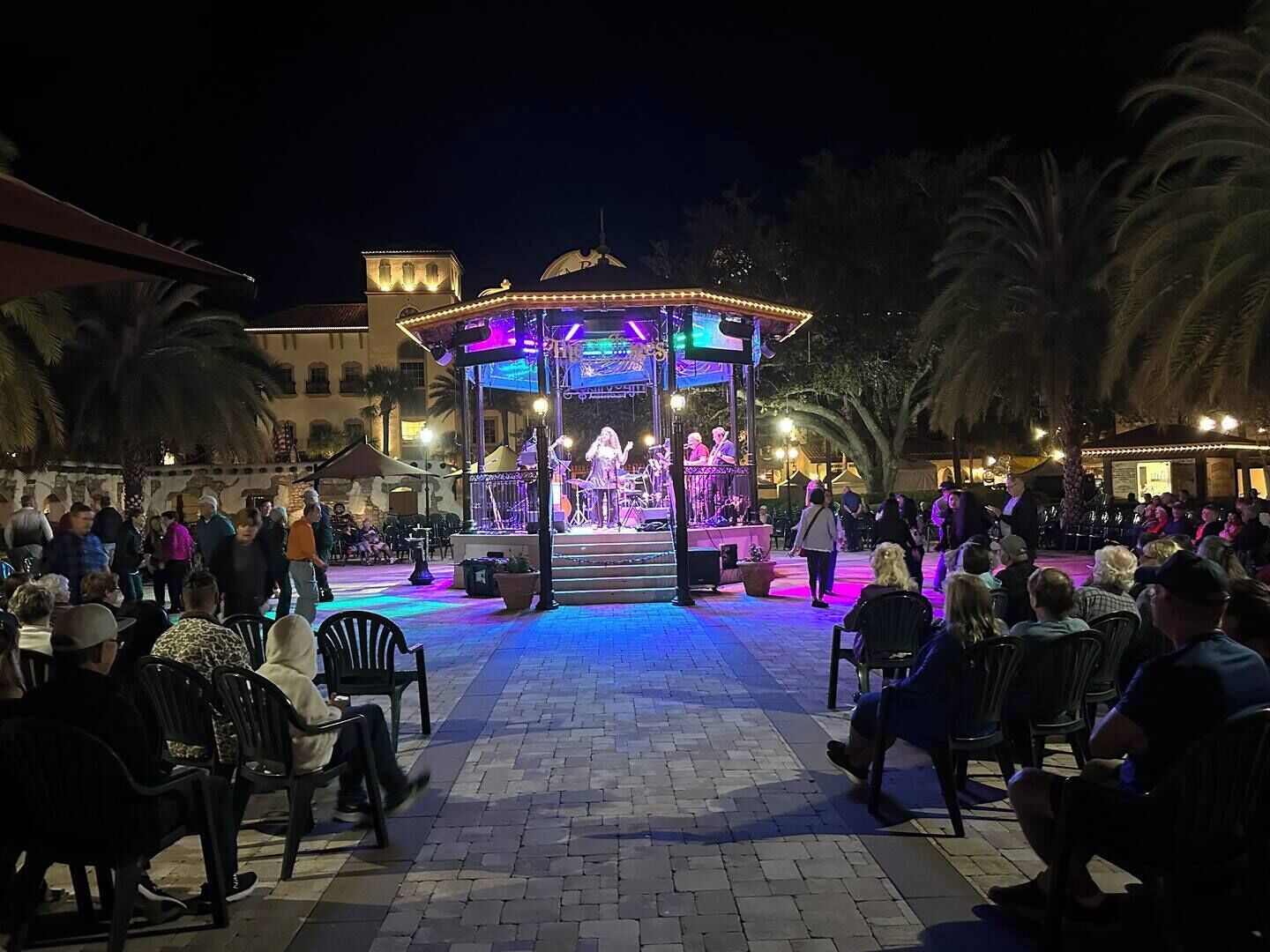 Un palco all'aperto con una band che si esibisce, circondato da un pubblico seduto.