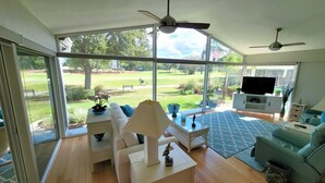 A spacious living room with large windows, a ceiling fan, a flat-screen TV, and a dining area. - 3/2 w/ Golf Cart in The Village of Santiago with Golf Course View! (The Villages)