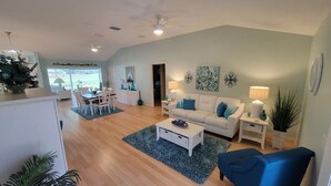 A spacious living room with a dining area, a white sofa, a blue armchair, and a coffee table. - 3/2 w/ Golf Cart in The Village of Santiago with Golf Course View! (The Villages)