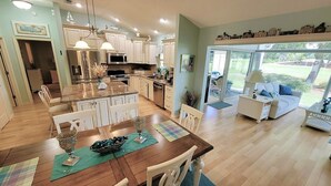 A spacious kitchen with a central island, white cabinetry, and a dining area with a wooden table. - 3/2 w/ Golf Cart in The Village of Santiago with Golf Course View! (The Villages)
