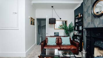 A living room with a leather sofa, a glass coffee table, and a bookshelf.