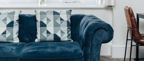 Un sofá azul con almohadas de estampado geométrico, un florero con flores y un sillón de cuero.