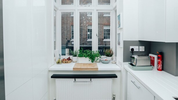 Eine moderne Küche mit weißen Schränken, einem großen Fenster, einer Holz Arbeitsplatte und einem Feuerlöscher auf der rechten Seite.