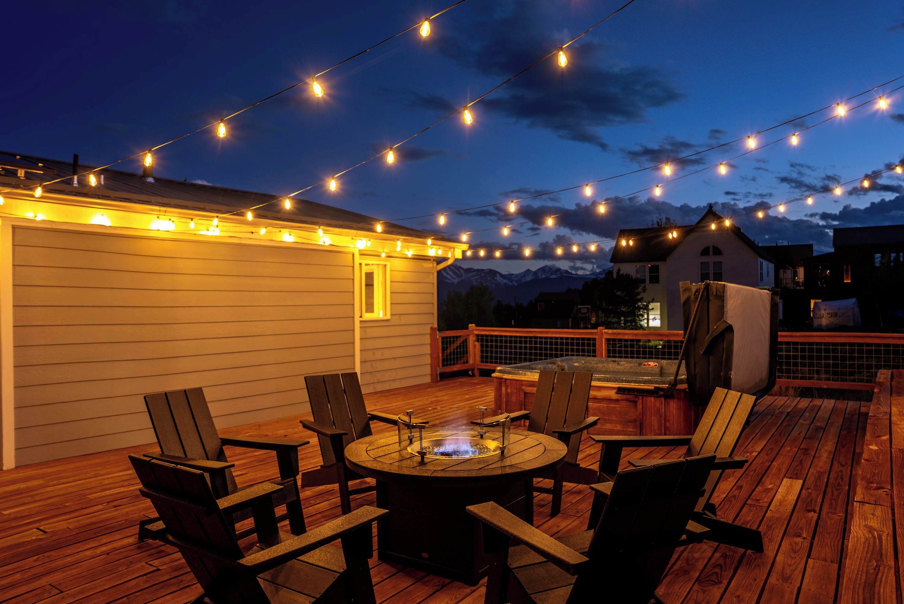 Eine Terrassenausstattung mit Feuerstelle, Holzstühlen und Lichterketten.