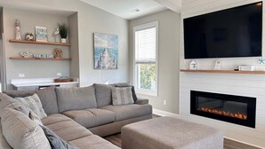 Una sala moderna con un sofá seccional, chimenea, televisor montado y estantes decorativos.