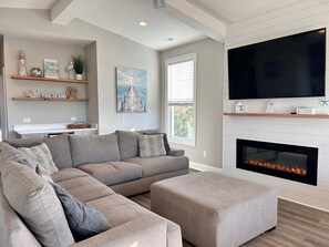 A modern living room with a sectional sofa, a fireplace, a mounted TV, and decorative shelves.