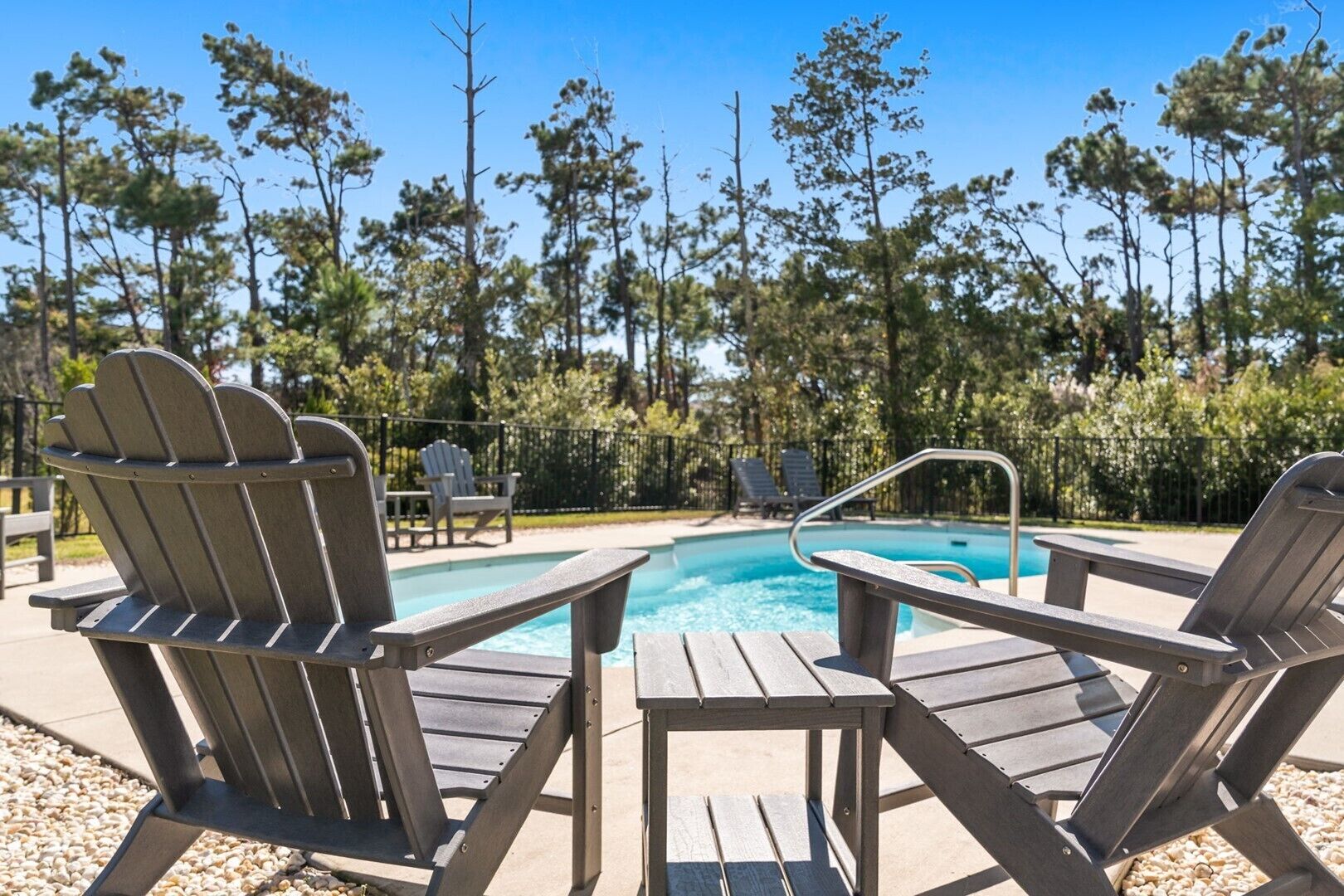 A poolside area with Adirondack chairs and a wooden table.