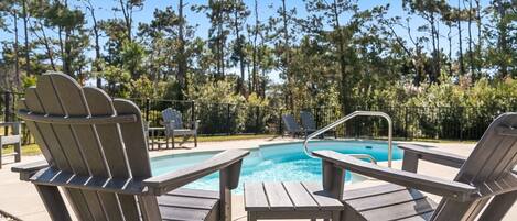 A poolside area with Adirondack chairs and a wooden table.