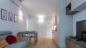 A modern kitchen with a dining area, a grey sofa with cushions, and a TV on a wooden cabinet. - Torino in corte by Wonderful Italy (Torino)