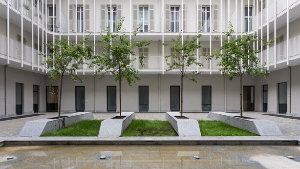 A courtyard with a central water feature, surrounded by a low wall and evenly spaced trees. - Torino in corte by Wonderful Italy (Torino)