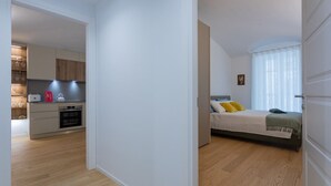 A modern apartment with a kitchen and a bedroom. The kitchen has a built-in oven and a microwave. The bedroom has a bed with a green blanket and yellow pillows. - Torino in corte by Wonderful Italy (Torino)