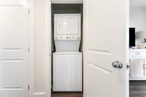 A laundry room with a stacked washer and dryer, a cabinet with a television, and a door with a silver handle.