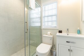 A modern bathroom with a glass shower enclosure, a toilet, and a sink with toiletries.