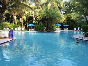 A clear swimming pool surrounded by palm trees and umbrellas, with lounge chairs and a small deck area. - Paradise Point by AvantStay | Golf Course Living (Key West)