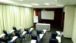 Une salle de conférence avec des rangées de chaises bleues, une table blanche et un tableau blanc.