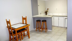Une cuisine compacte comprenant une table à manger et deux tabourets, un plan de travail blanc et des placards.