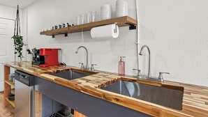 Une cuisine équipée de deux éviers, de plans de travail en bois, d’une machine à café et d’une étagère où sont rangées des tasses et un rouleau d’essuie-tout.