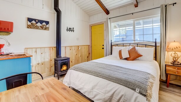 A cozy bedroom with a bed, a wooden desk, a stove, and a window. - Tahoe Mountain Inn #3 (South Lake Tahoe)