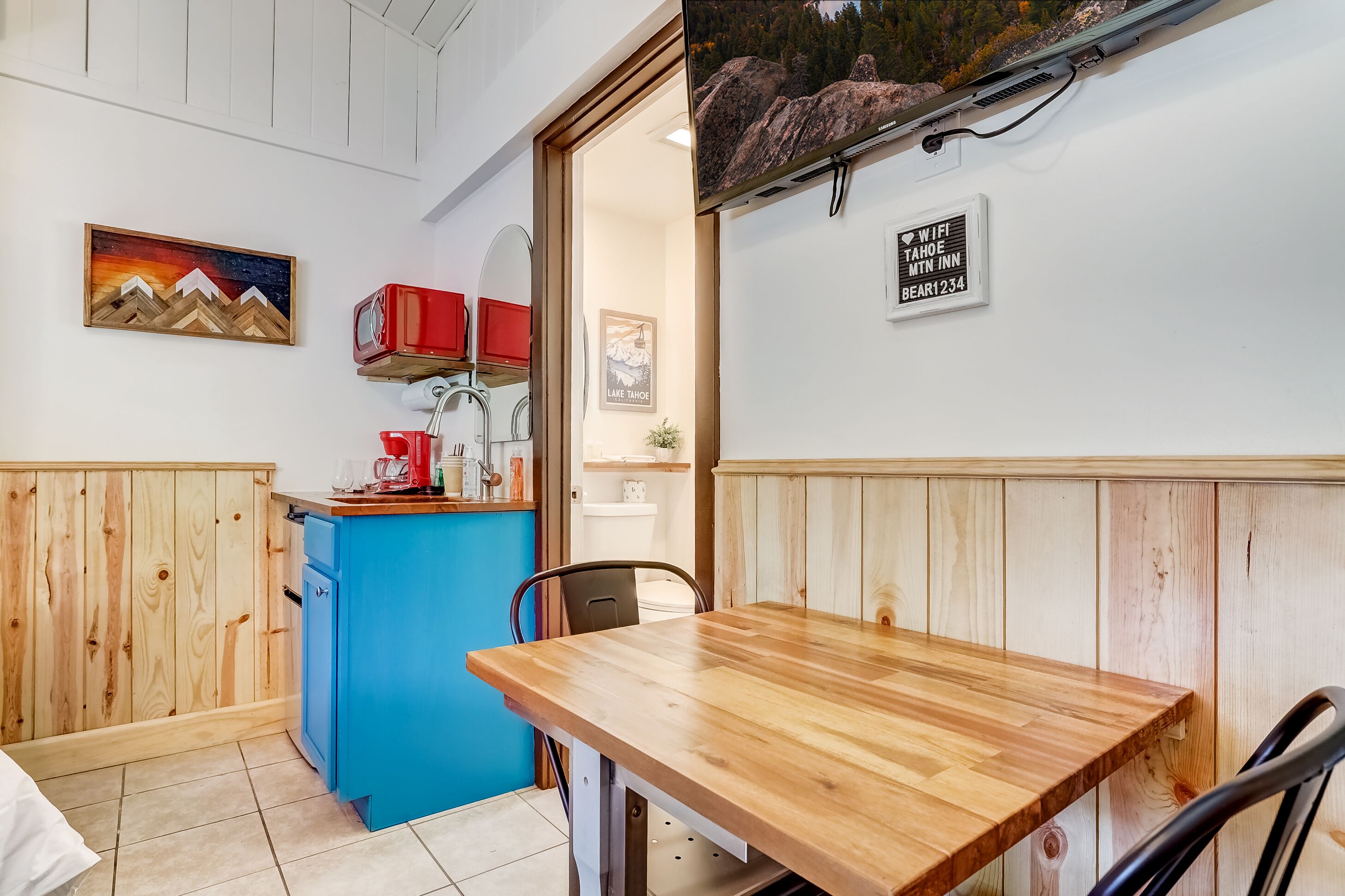 Una mesa de comedor de madera con un armario azul y un electrodoméstico rojo en una habitación con paneles de madera.