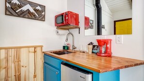 A compact kitchen with a wooden countertop, a sink, a red coffee maker, and a microwave on a shelf.