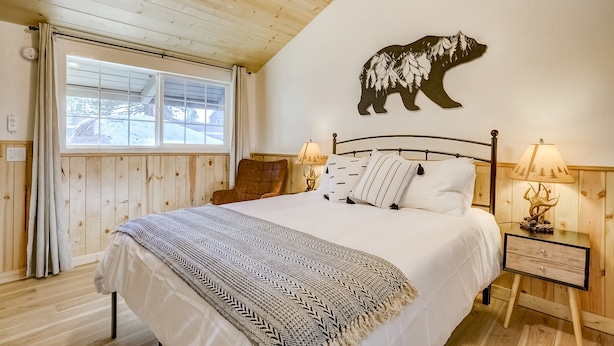 Une chambre confortable avec un grand lit, des murs en bois, une décoration murale représentant un ours, deux lampes de chevet et une fenêtre avec des rideaux.