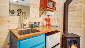 Cocina compacta con encimera de madera, un lavabo, microondas, cafetera y estufa a leña.