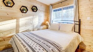 Un dormitorio con paneles de madera, una cama, dos decoraciones hexagonales en la pared, una ventana con cortinas y una mesita de noche con lámpara.