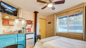A cozy cabin room with a bed, a small kitchenette, a ceiling fan, and a window with a view of a snowy landscape. - Tahoe Mountain Inn #9 (South Lake Tahoe)