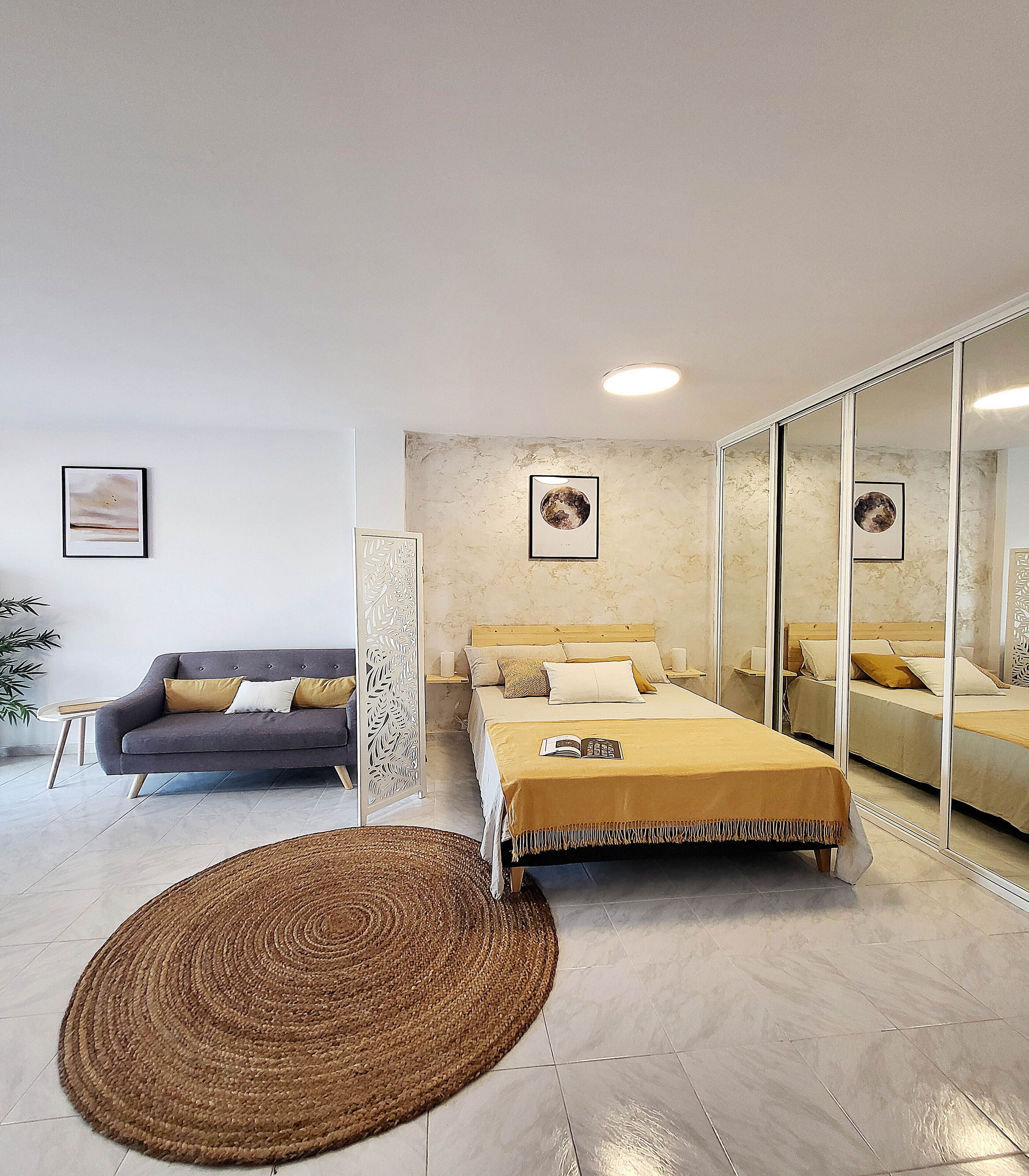 Une chambre à coucher moderne avec un lit, un canapé, un grand miroir et des œuvres d’art accrochées aux murs.