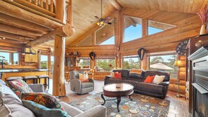 Un intérieur spacieux de chalet en bois, doté d’une cheminée, de grandes fenêtres et d’un coin salon confortable.
