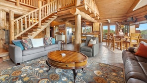 Un intérieur spacieux de chalet en bois, agrémenté d’un magnifique escalier, d’un coin repas et d’un salon confortable avec une grande table basse ronde.