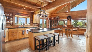 Une cuisine spacieuse avec des meubles en bois, un îlot central doté de tabourets, une grande fenêtre et un luminaire suspendu.