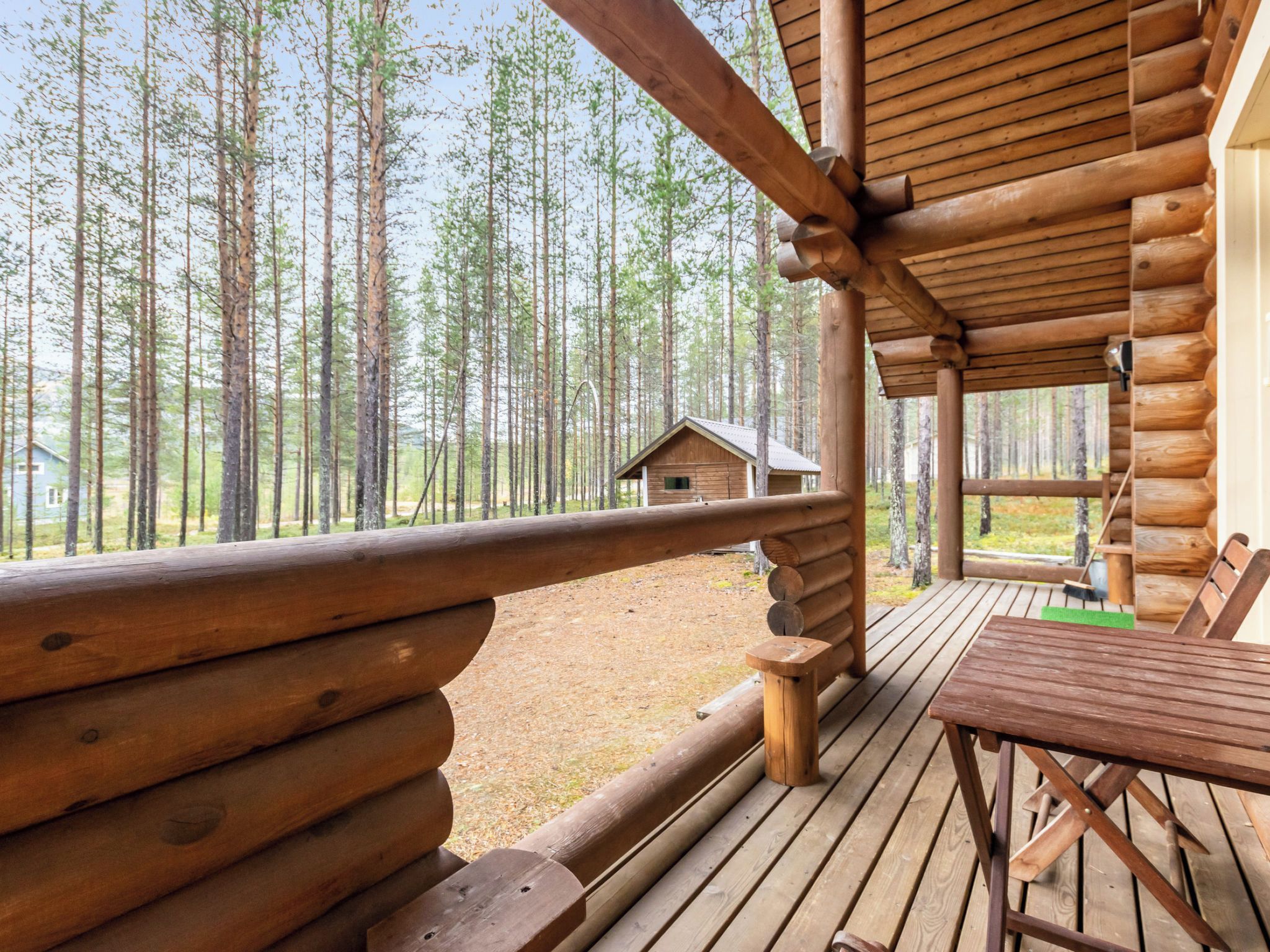 A wooden deck with a view of a forest and a small cabin in the distance.