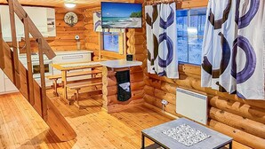 Un chalet confortable aux murs en bois, avec un escalier en bois, un coin repas, une cuisine et une fenêtre donnant sur la plage.