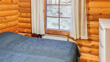 Ein Schlafzimmer in einer Blockhütte mit einem Bett, einem Schminktisch und einem Fenster mit Vorhängen.