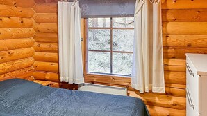 Une chambre dans un chalet en rondins, avec un lit, une commode et une fenêtre avec des rideaux.