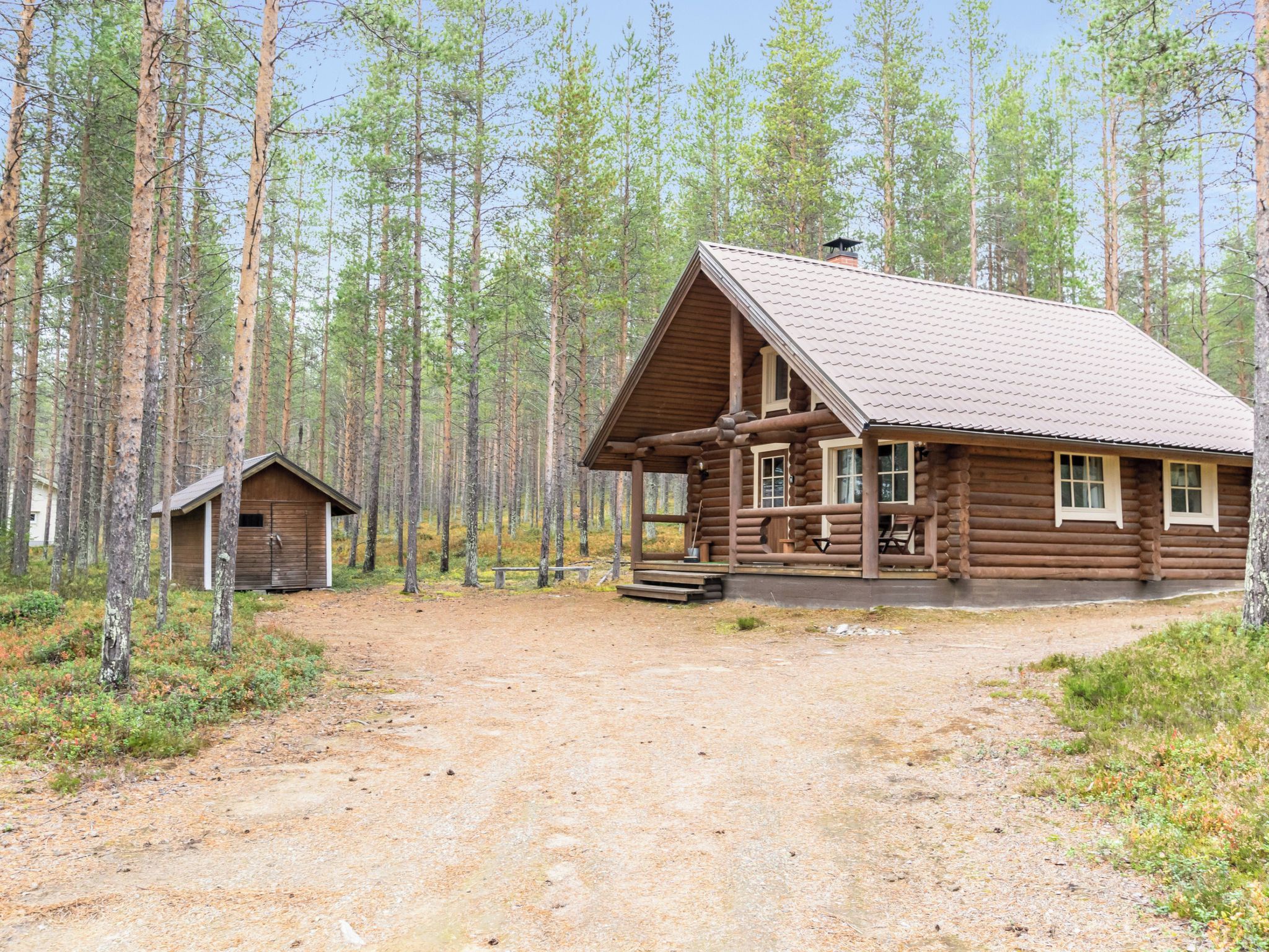 Hirsimökki, jossa on kuisti, ja pienempi mökki metsäisellä alueella.