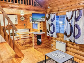 A cabin interior with a wooden staircase, a dining table, a bench, a sink, and a window with curtains.